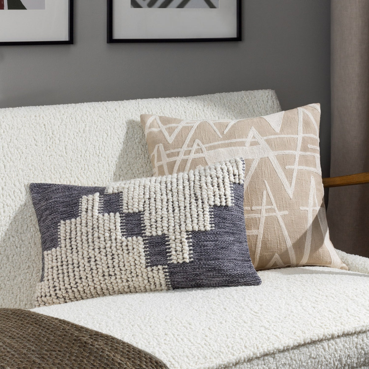Himal Abstract Cotton Cushion in Dusk, an oblong lumbar cushion with a stepped grey and cream design mixing flat weave and raised loop texture, shown on a white sofa beside a beige patterned cushion.