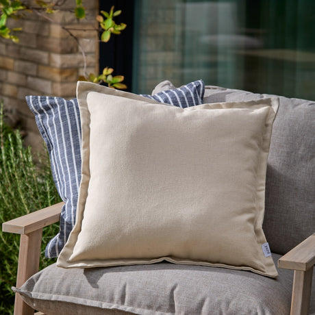 Holmfirth Canvas Plain Cotton Cushion in natural with flat oxford border, shown on a grey outdoor sofa beside a blue and white striped cushion.