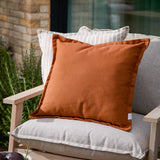 Holmfirth Canvas Plain Cotton Cushion in pecan orange, a square cushion with piped edges, shown on a light grey outdoor sofa alongside striped scatter cushions.