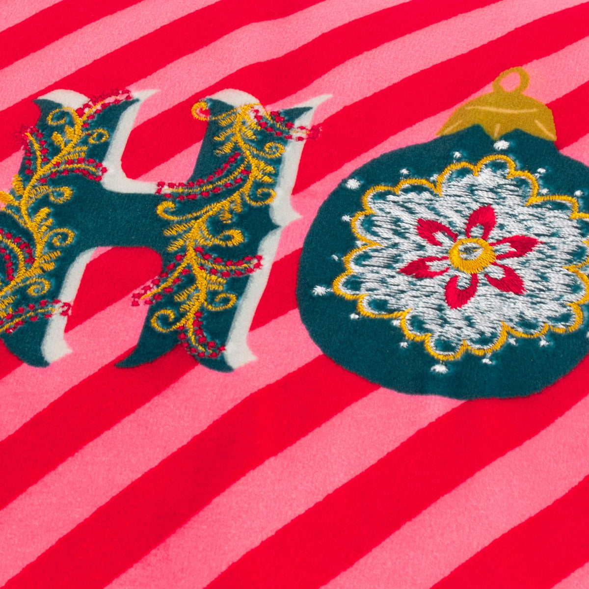 Close-up of the HoHoHo Abstract Velvet Cushion in red, showing embroidered "HO" lettering and a bauble motif on a red and pink candy-striped velvet ground.