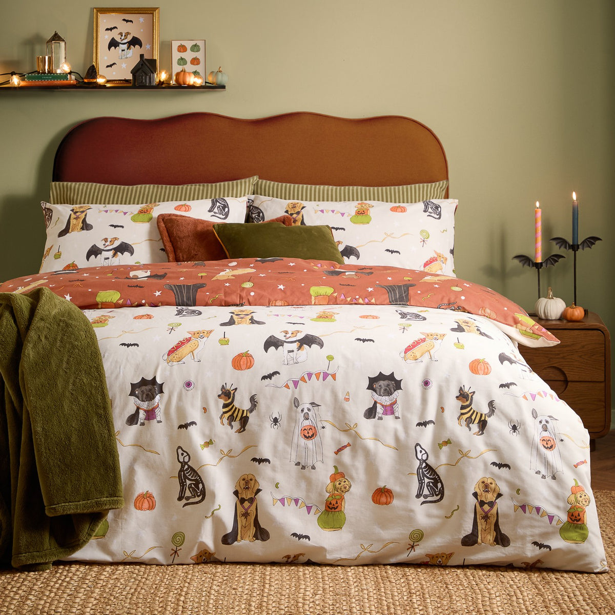 Reversible Howl-O-Ween duvet set with cream side featuring dogs in Halloween costumes and rust side with bat and star print, shown with matching pillowcases in a green bedroom.