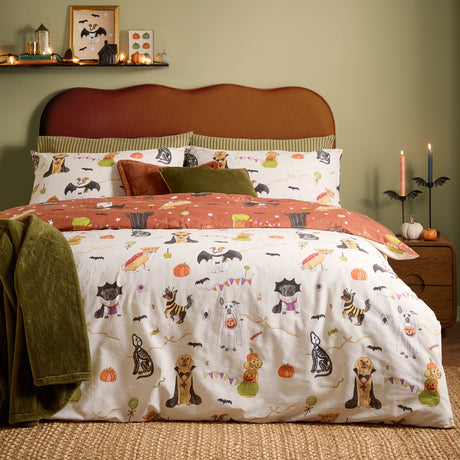 Reversible Howl-O-Ween duvet set with cream side featuring dogs in Halloween costumes and rust side with bat and star print, shown with matching pillowcases in a green bedroom.