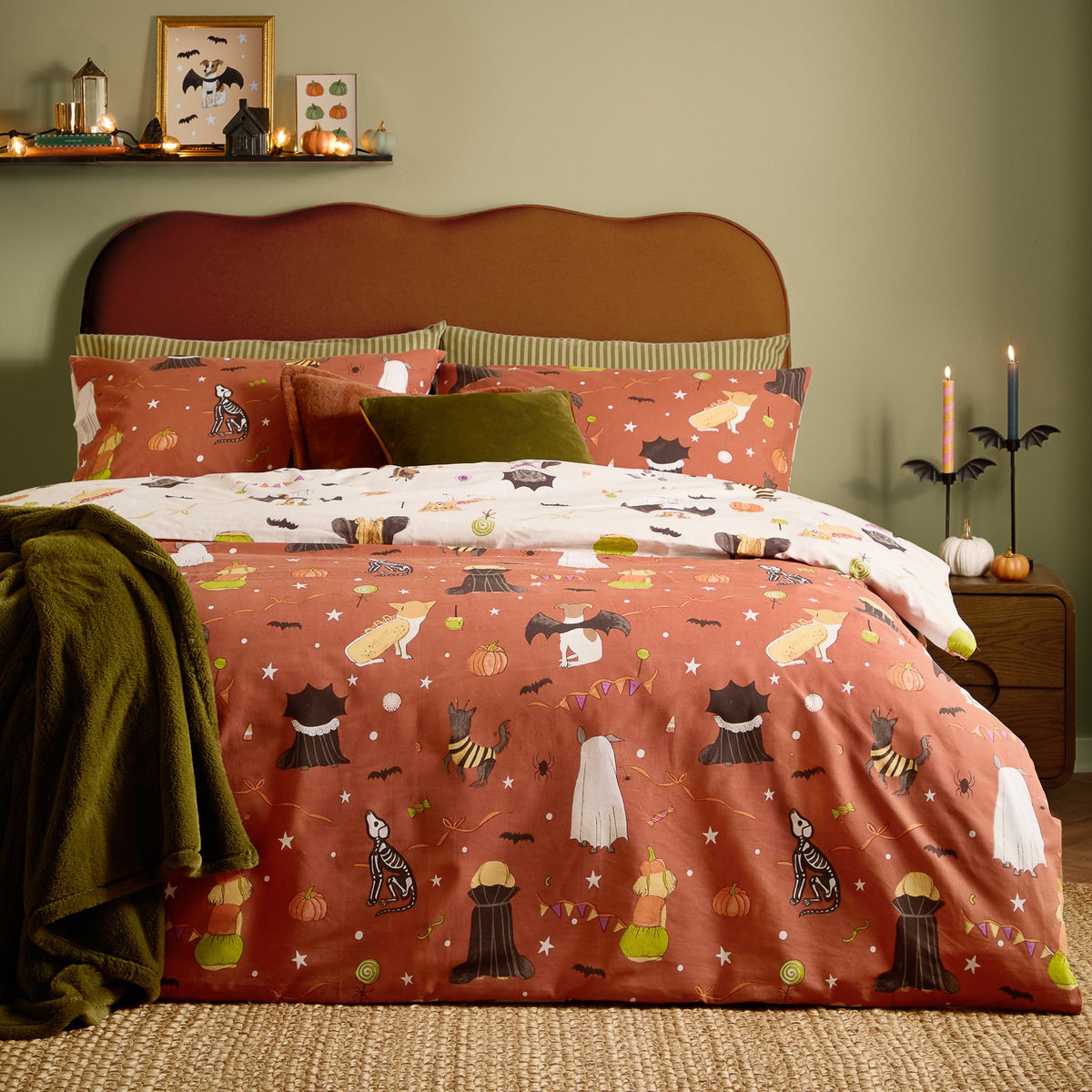 Howl-O-Ween Reversible Animal Duvet Cover Set on a bed, rust and cream cotton fabric printed with dogs in Halloween costumes, styled with olive cushions and throw in a green bedroom.
