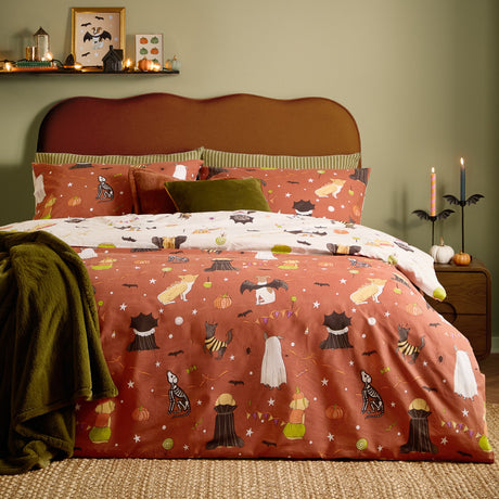 Howl-O-Ween Reversible Animal Duvet Cover Set on a bed, rust and cream cotton fabric printed with dogs in Halloween costumes, styled with olive cushions and throw in a green bedroom.