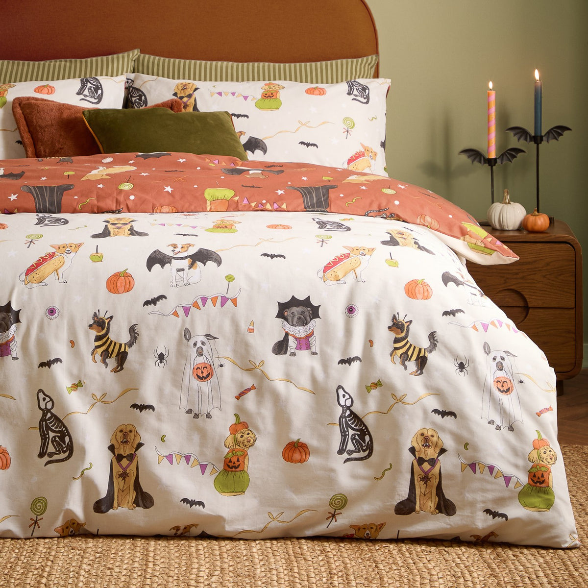 Howl-O-Ween reversible duvet cover set on a bed, cream cotton fabric printed with dogs in Halloween costumes, paired with a rust-toned reverse and matching pillowcases in a bedroom setting.