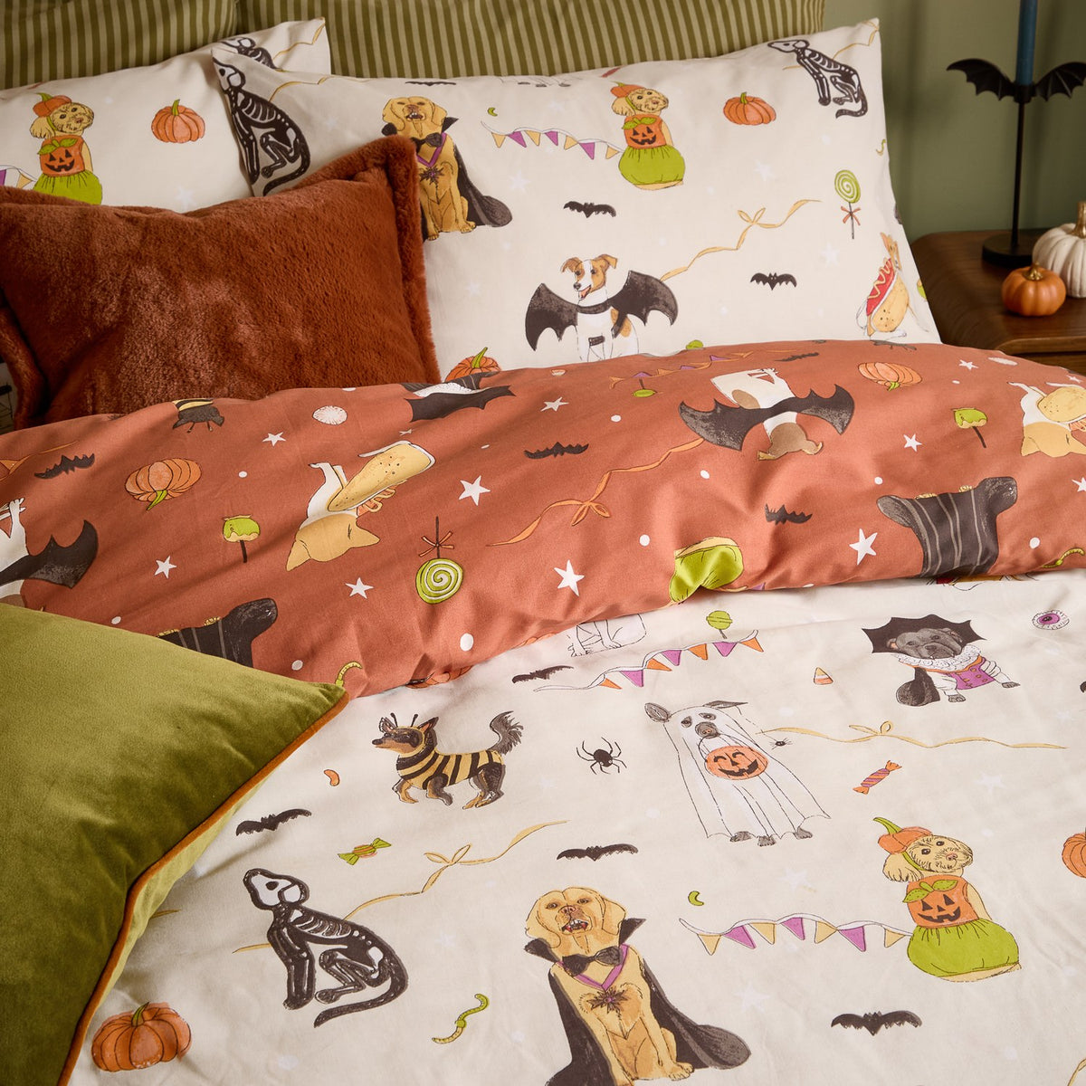 Howl-O-Ween reversible duvet cover set on a bed, cream side printed with dogs in Halloween costumes and rust reverse with bat and pumpkin motifs, styled with matching pillowcases and cushions.