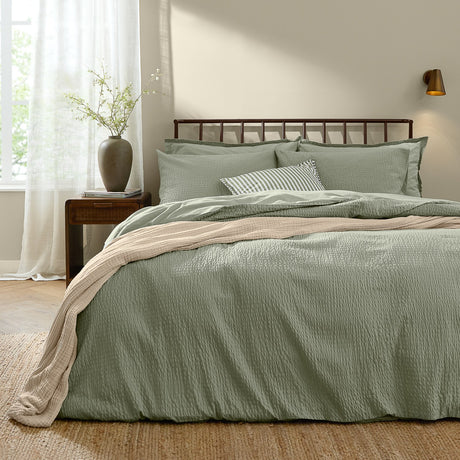 Hebden Cotton Plain Duvet Cover Set in bay green with matching pillowcases, seersucker texture, on a bed with dark headboard in a bedroom setting.