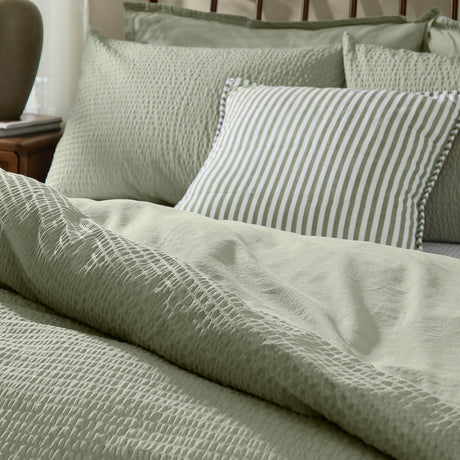 Hebden Cotton Plain Duvet Cover Set in bay green, showing the seersucker-textured cover and matching pillowcases on a bed with a striped accent cushion.