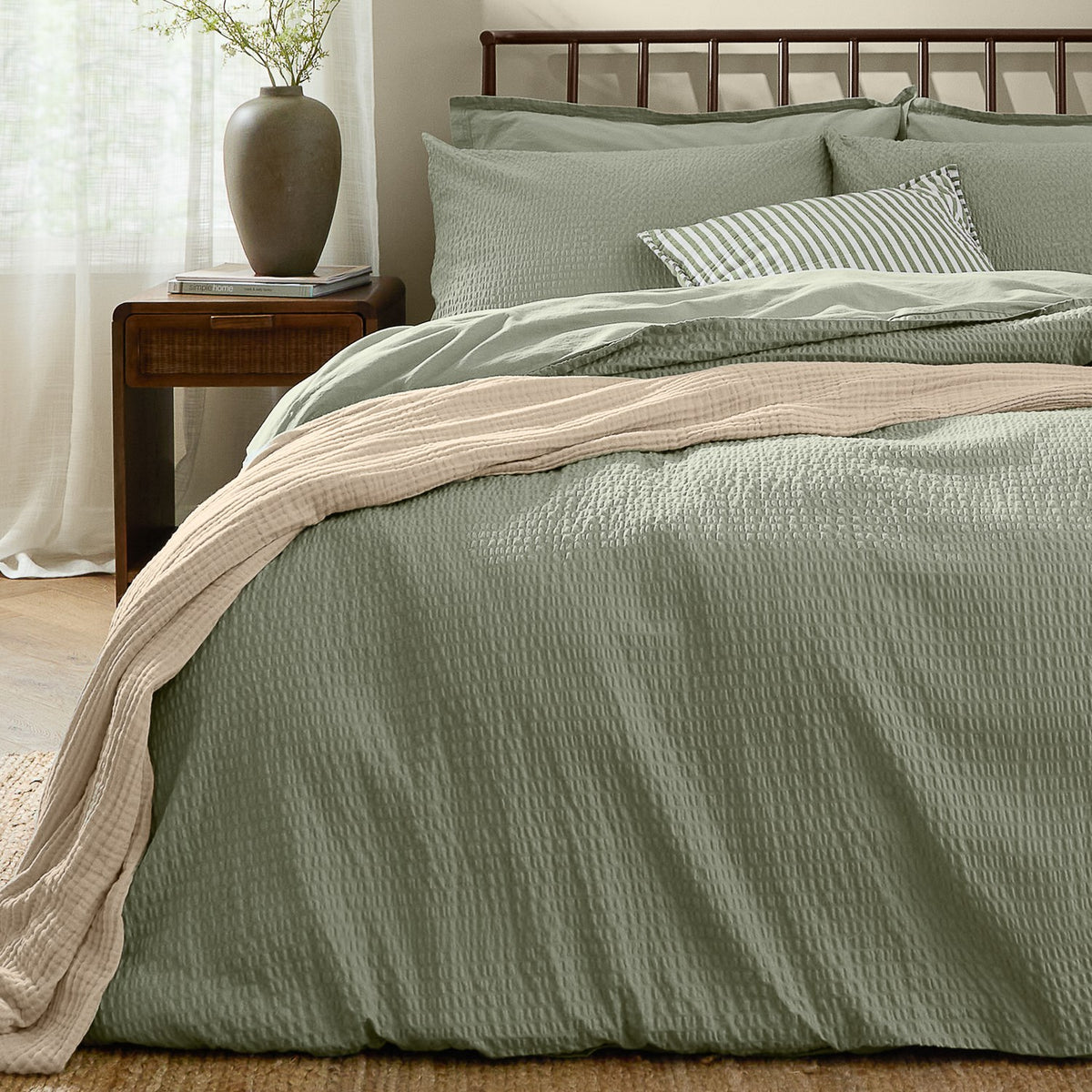 Hebden Cotton Plain Duvet Cover Set in bay green with seersucker texture, styled on a bed with matching pillowcases, striped cushion, and beige throw in a bedroom setting.