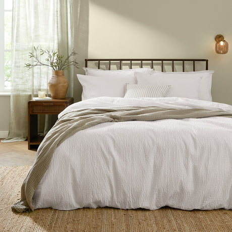 Hebden Cotton Plain Duvet Cover Set in Chalk white with textured seersucker finish, styled on a bed with matching pillowcases and a striped cushion in a bedroom setting.