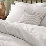 Hebden Cotton Plain Duvet Cover Set in Chalk, textured white seersucker bedding with matching pillowcases and a grey striped cushion, styled on a bed.