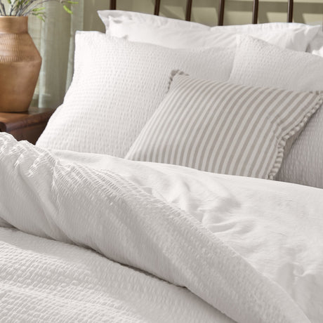 Hebden Cotton Plain Duvet Cover Set in Chalk, textured white seersucker bedding with matching pillowcases and a grey striped cushion, styled on a bed.