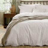 Hebden Cotton Plain Duvet Cover Set in Chalk white with seersucker texture, styled on a bed with white pillows and a striped throw in a bedroom setting.