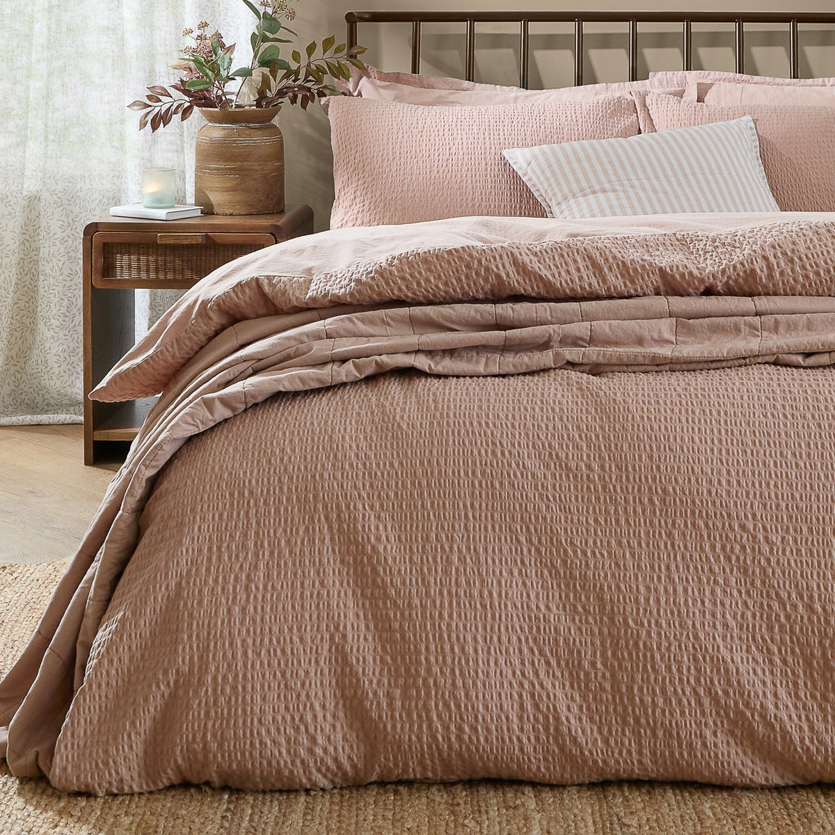 Hebden Cotton Plain Duvet Cover Set in Cotta pink seersucker texture, dressed on a bed with matching pillowcases and a striped cushion in a bedroom setting.