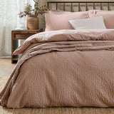 Hebden Cotton Plain Duvet Cover Set in Cotta pink seersucker texture, dressed on a bed with matching pillowcases and a striped cushion in a bedroom setting.