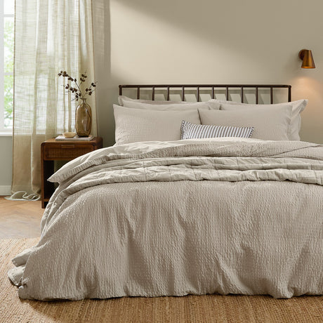 Hebden Cotton Plain Duvet Cover Set in stone, showing a seersucker-textured cover with matching pillowcases on a bed in a neutral-toned bedroom.
