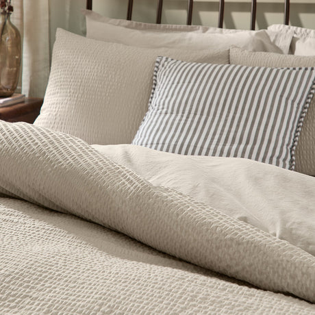 Hebden Cotton Plain Duvet Cover Set in stone, showing textured seersucker-face pillowcases and duvet cover styled on a bed with a striped accent cushion.