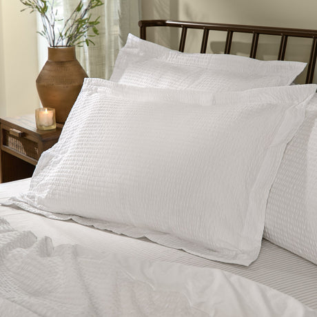 Hebden Percale Cotton Pillowcase Pair in Chalk, styled on a bed with textured seersucker-faced covers against dark metal headboard in a bedroom setting.