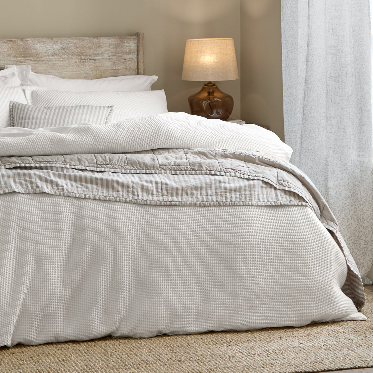 Hebden Cotton Plain Duvet Cover Set in Chalk on a bed with waffle-textured cotton front, styled with striped pillowcases in a neutral bedroom setting.