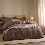 Hebden Cotton Plain Duvet Cover Set in Cocoa Brown on a bed with striped trim detail, wooden headboard, and neutral bedroom setting.