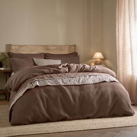 Hebden Cotton Plain Duvet Cover Set in Cocoa Brown on a bed with striped trim detail, wooden headboard, and neutral bedroom setting.