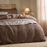 Hebden Cotton Plain Duvet Cover Set in Cocoa Brown, waffle-textured cotton bedding with striped percale trim, styled on a bed in a warm-toned bedroom setting.