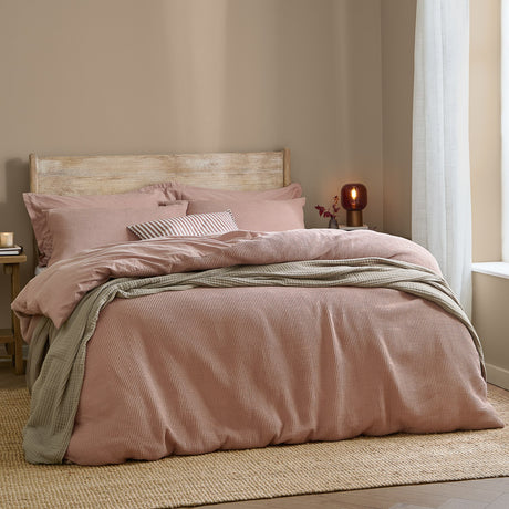 Hebden Cotton Plain Duvet Cover Set in Cotta dusky pink, waffle-weave finish, shown on a bed with striped cushions in a neutral bedroom setting.