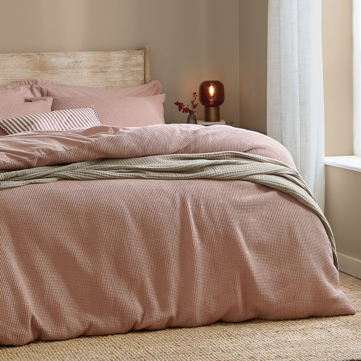 Hebden Cotton Plain Duvet Cover Set in Cotta dusky pink, waffle-weave cover with striped and plain pillowcases on a bed in a neutral-toned bedroom.