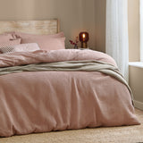 Hebden Cotton Plain Duvet Cover Set in Cotta dusky pink, waffle-weave cover with striped and plain pillowcases on a bed in a neutral-toned bedroom.