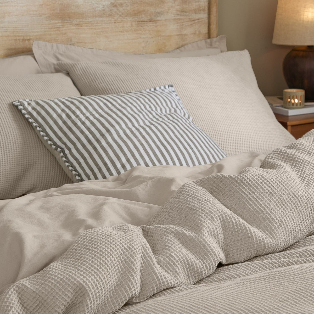 Hebden Cotton Plain Duvet Cover Set in Stone, waffle-textured cotton bedding with a striped cushion, styled on a bed in a bedroom setting.