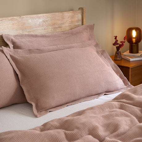 Hebden Percale Cotton Pillowcase Pair in Cotta dusky pink, waffle-textured cotton shams on a bed with wooden headboard, styled with a matching bedspread and bedside lamp.