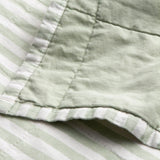 Close-up of the Hebden Percale Cotton Bedspread in Eucalyptus/Bay Green, showing quilted stitching where the plain green face meets the reversible green-and-white striped edge.
