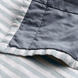 Close-up of the reversible Hebden Percale Cotton Bedspread, showing the denim-blue cotton face folded back over the pale mineral-blue and white striped side with visible stitching.