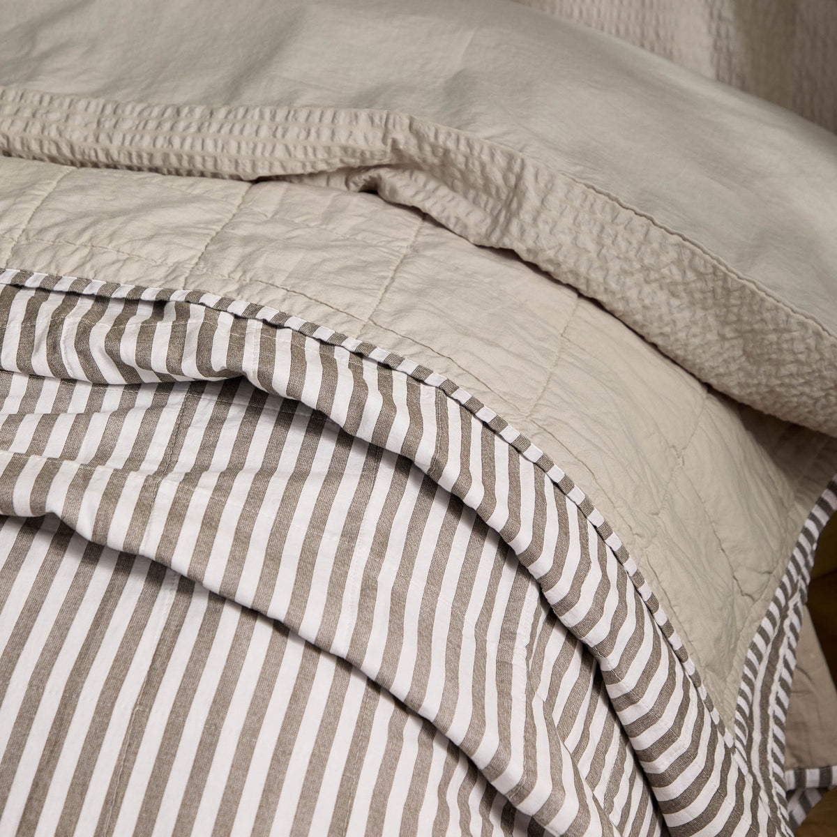 Hebden Percale Cotton Bedspread in Mole/Stone, folded to show mole-and-white stripe on one side and quilted stone reverse in square-grid stitching.