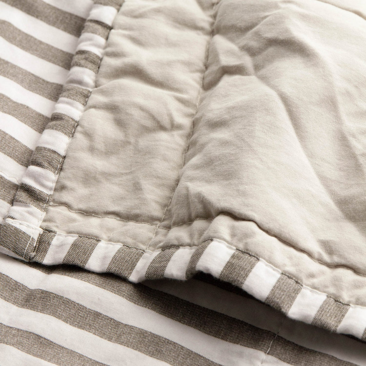 Close-up of the Hebden Percale Cotton Bedspread in Mole/Stone, showing the reversible design with mole and white striped edging against a quilted stone percale side.