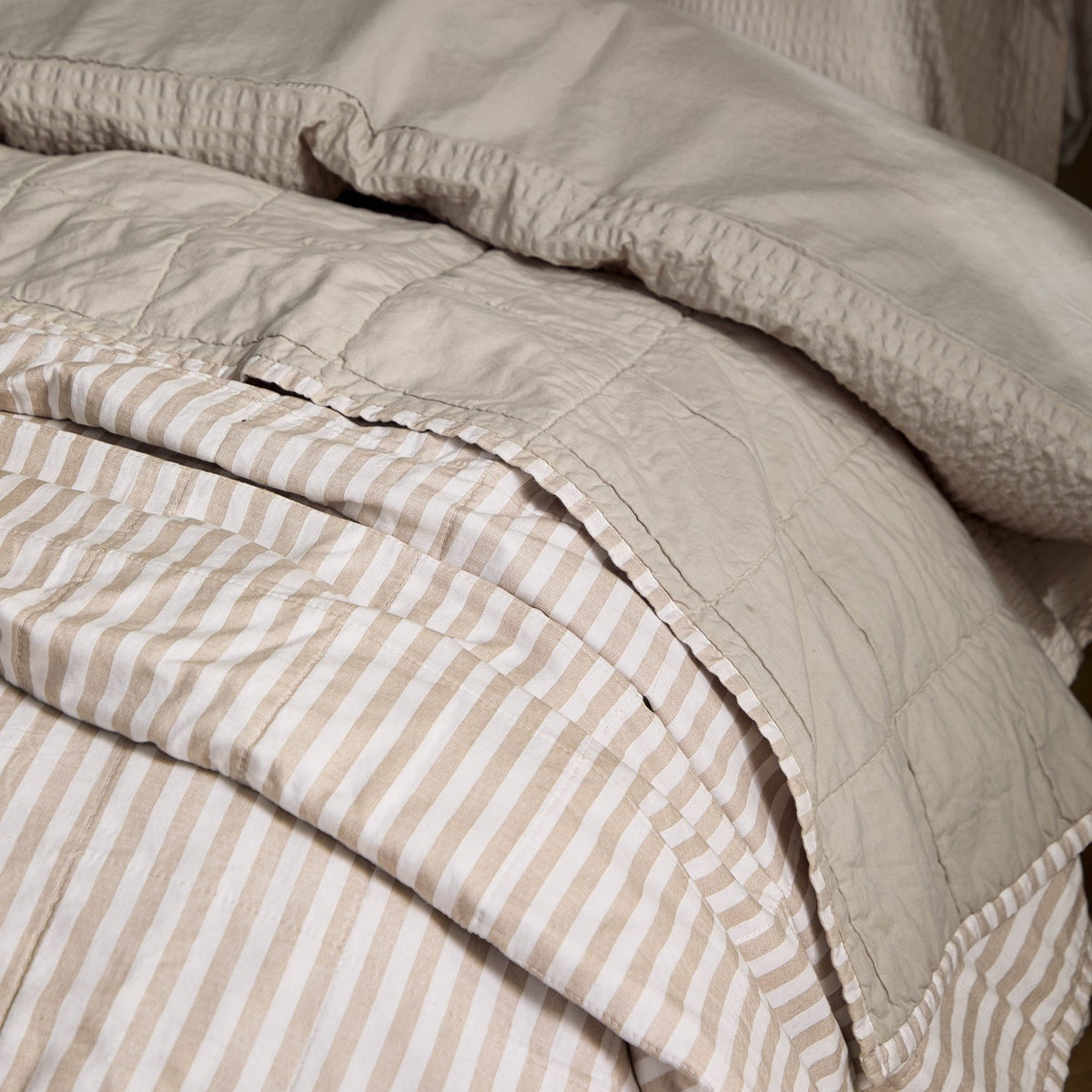 Hebden Percale Cotton Bedspread in Natural/Stone, close-up showing reversible beige-and-white striped side folded back over the plain stone cotton reverse.