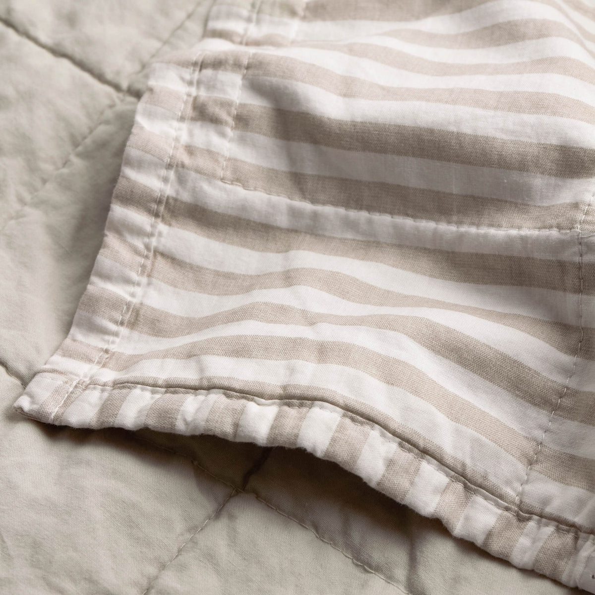 Hebden Percale Cotton Bedspread corner detail showing beige and white striped reverse against the plain stone quilted side, in 100% cotton.
