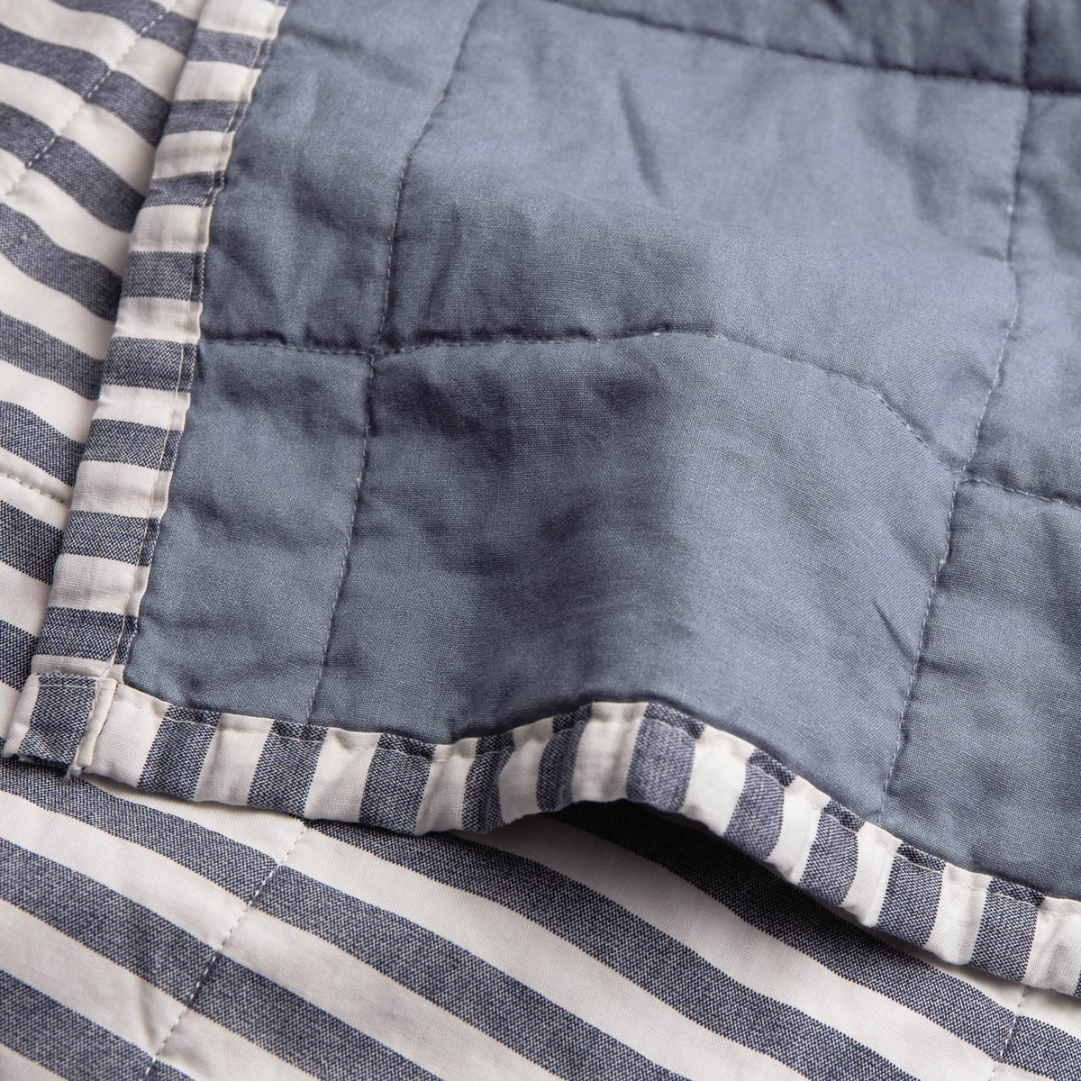 Close-up of the Hebden Percale Cotton Bedspread in Navy/Denim Blue, showing the quilted plain denim blue percale side folded back to reveal the navy and white striped reverse and edge binding.