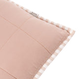 Close-up of the Hebden Percale Cotton Cushion corner in blush, showing plain cotton front, gingham-check border, and striped piped edge with fabric label.