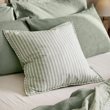 Hebden Percale Cotton Cushion in Eucalyptus/Bay Green stripe, 55cm square with piped edge, styled on a bed with sage waffle pillows and layered green bedding.