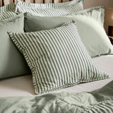 Hebden Percale Cotton Cushion in Forest/Bay Green stripe, shown on a bed layered with sage green pillows, shams, and bedding in a bedroom setting.