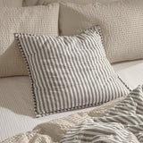 Hebden Percale Cotton Cushion in Mole grey and white stripe with quilted grid and Oxford-style border, shown on a bed with striped sheets and textured cream pillows.