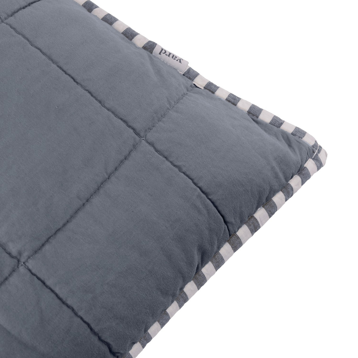 Close-up of the Hebden Percale Cotton Cushion in denim blue, showing box-stitched quilting and a striped navy and cream edge trim with fabric brand tag.