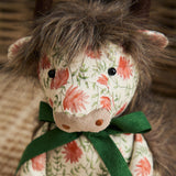 Hugo Polyester Door Stop shaped as a highland cow, close-up of shaggy brown mane, dark eyes, muted-grey muzzle, cream floral fabric body and green ribbon bow.