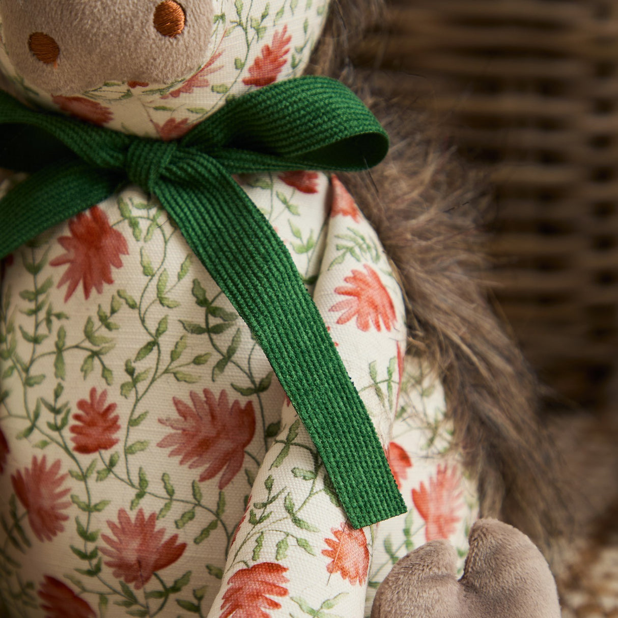 Close-up of the Hugo Polyester Door Stop, a highland cow shaped in coral and rust floral fabric with a forest-green ribbon bow, shaggy grey mane, and soft muzzle.