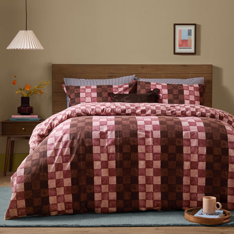Huxley Reversible Check Duvet Cover Set in chocolate, dusky rose and blush checkerboard print, dressed on a bed with striped pillowcases in a modern bedroom setting.