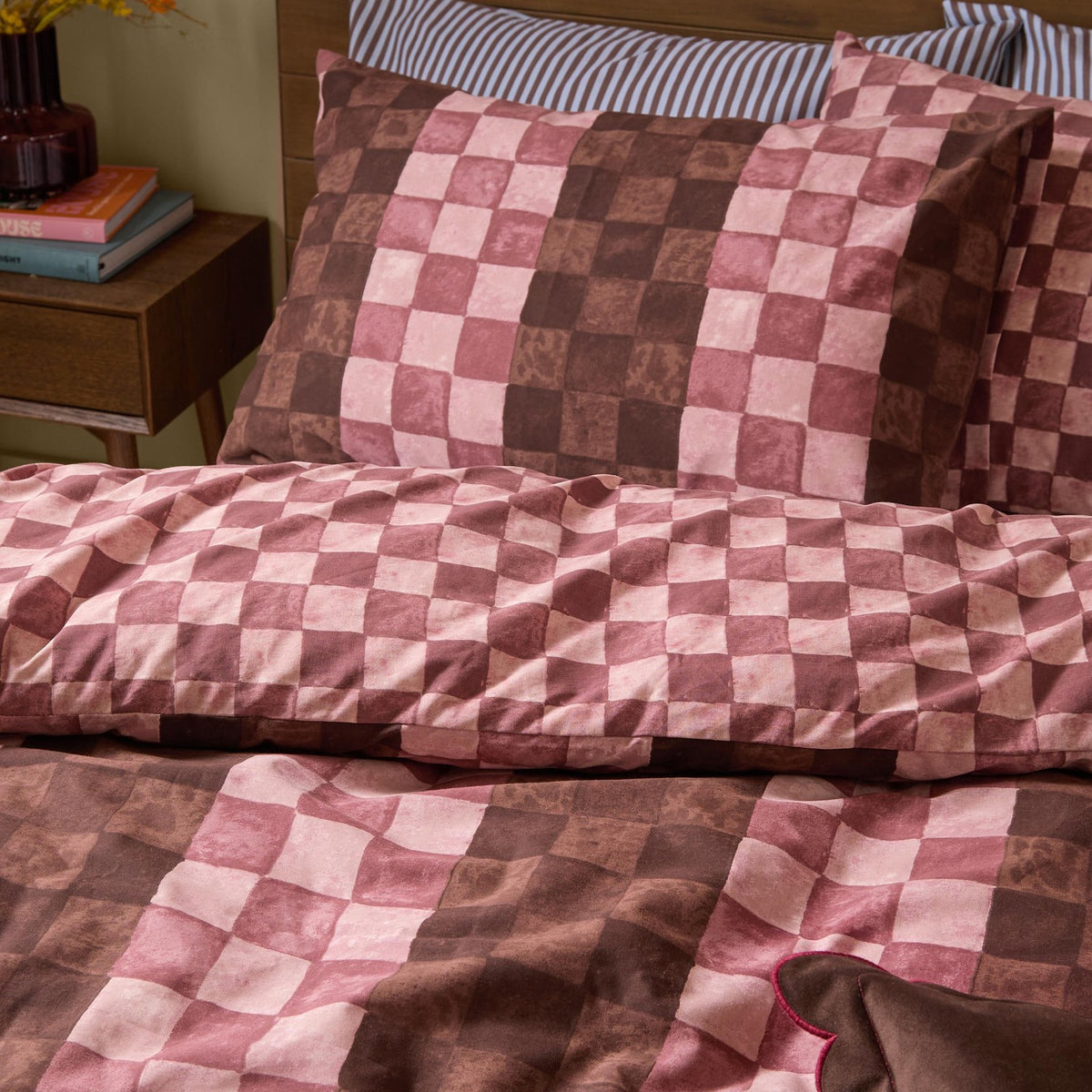 Huxley Reversible Check Duvet Cover Set in chocolate, dusky rose and blush, shown on a bedroom bed with matching pillowcases against a striped inner pillow.