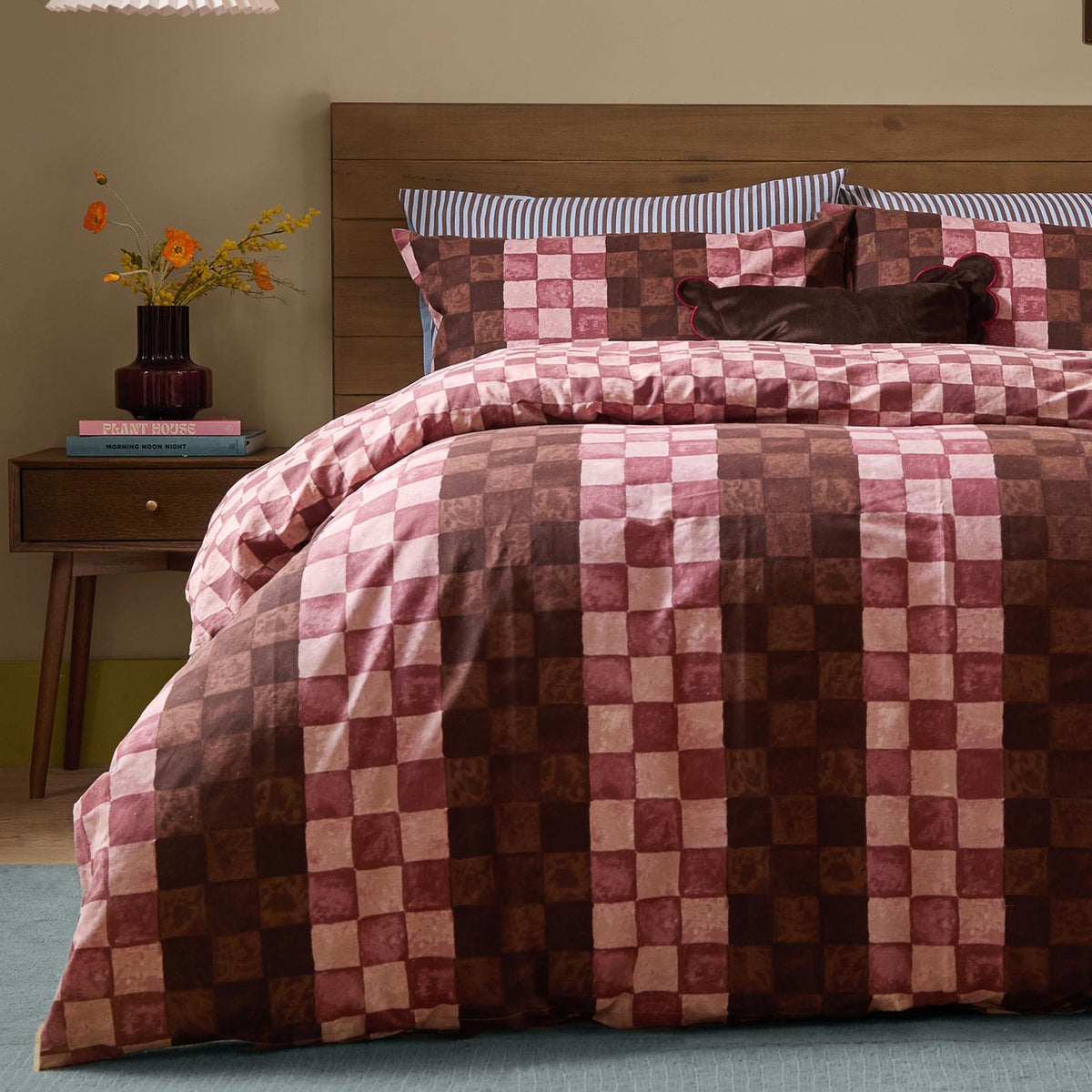 Huxley Reversible Check Duvet Cover Set in Chocolate & Blush, shown on a bed with striped pillowcases and a dark cushion in a bedroom setting with a wooden headboard and side table.