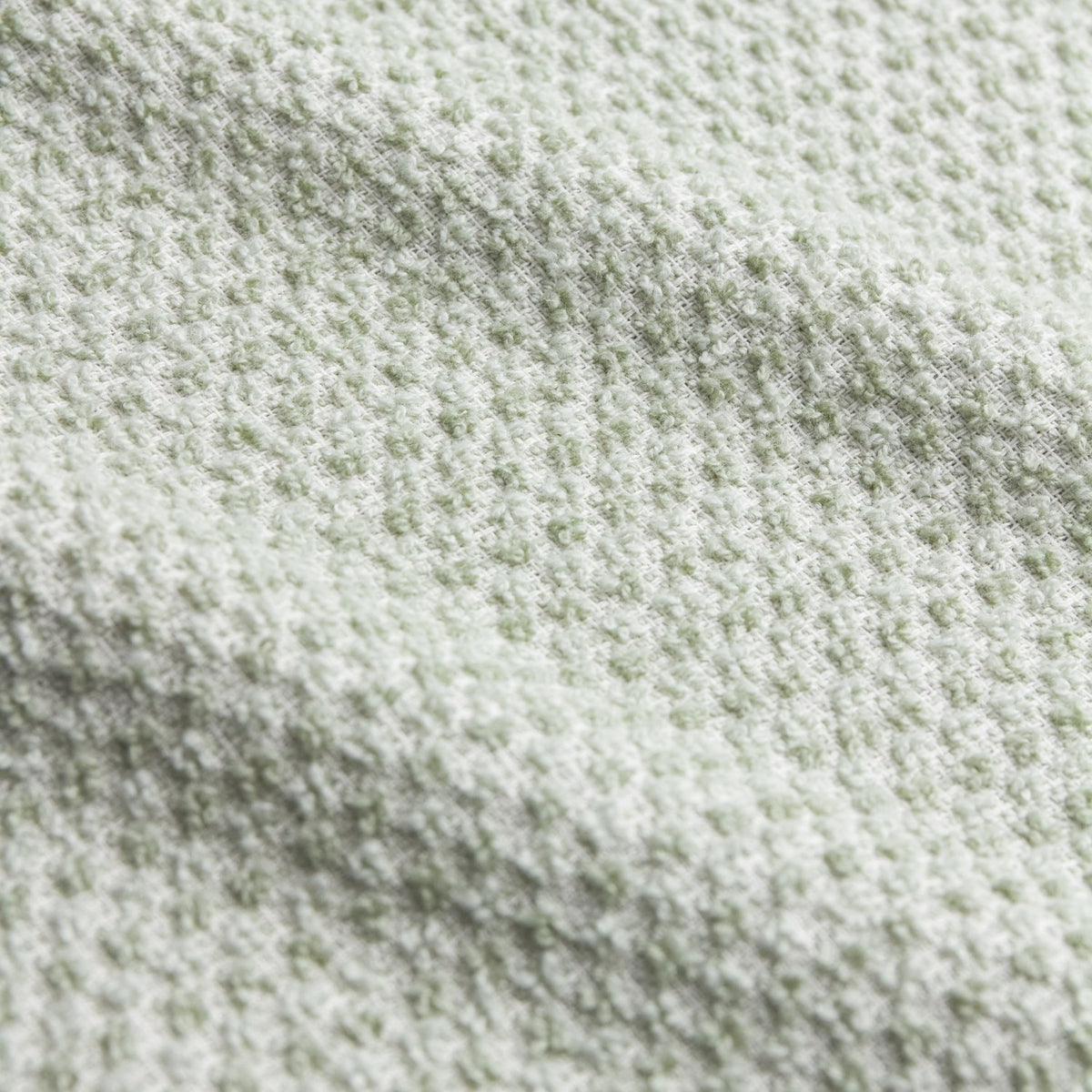 Close-up of the Hebden Plain Cotton Towels in Bay Green, showing a textured waffle-weave cotton surface with pale, near-white flecks.