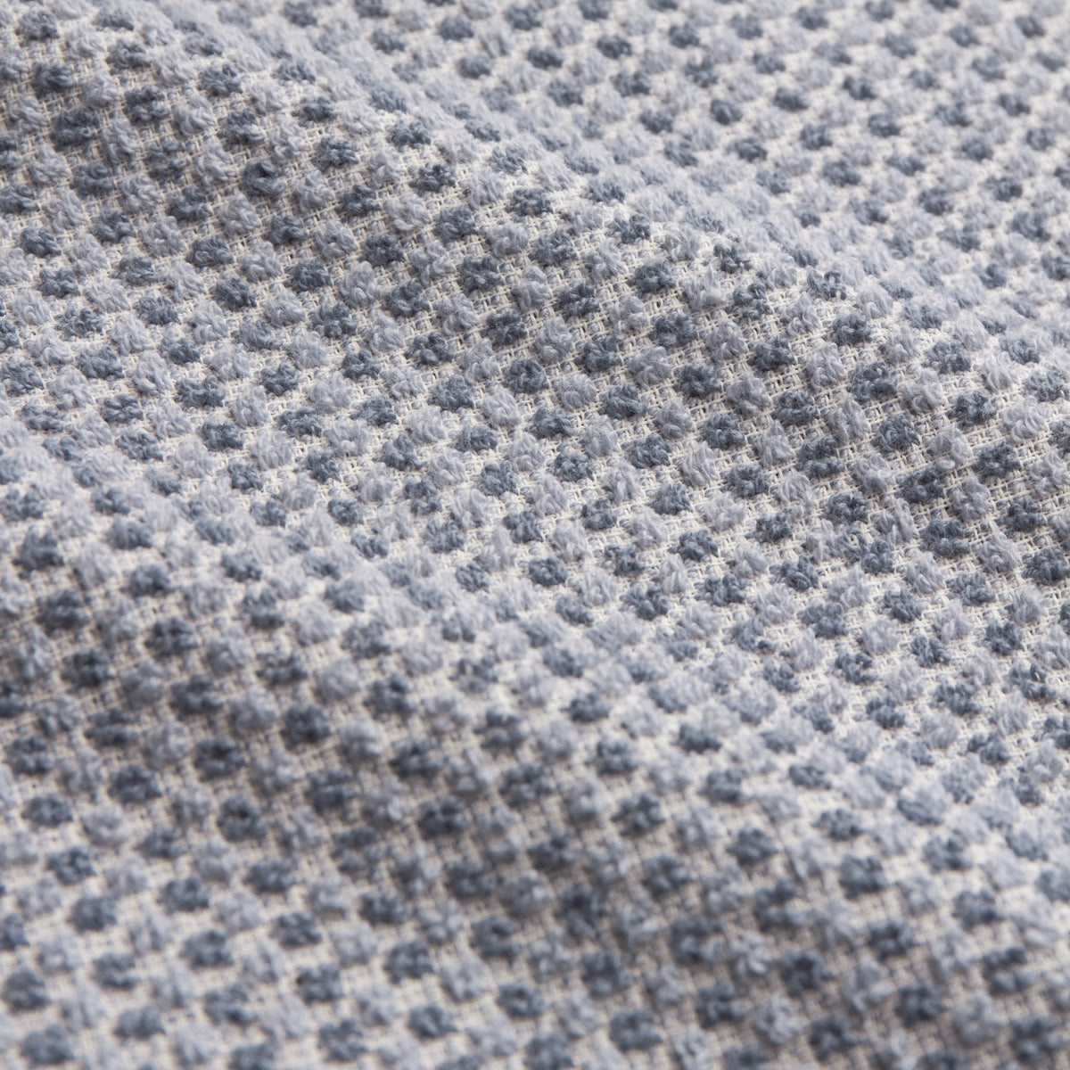 Close-up of Hebden Plain Cotton Towel in denim blue, showing the woven waffle texture with raised cotton pockets in a soft blue and pale grid pattern.